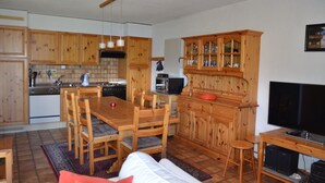 A compact kitchen with wooden cabinets, a dining table, and a TV.