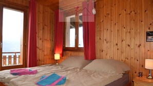 A wooden cabin room with a bed, a nightstand, and a window with curtains.