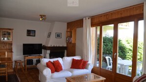 Ein Wohnzimmer mit einem weißen Sofa, roten Kissen, einem Holztisch, einem Fernseher und einem Kamin.