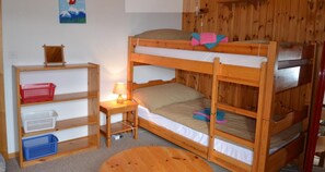 Een slaapkamer met een stapelbed, een houten vloer, een klein tafeltje met een lamp en een plank met manden.