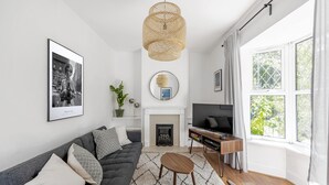 Un salon moderne avec un canapé gris, une table basse ronde en bois, une cheminée, un téléviseur et une grande fenêtre avec des rideaux.