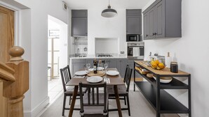 Une cuisine moderne avec des meubles gris, une table à manger en bois pour quatre personnes et un four encastré.