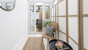 Une pièce avec un fauteuil en osier, une table noire sur laquelle se trouve un livre, et un grand miroir accroché au mur.