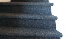 Un escalier aux marches sombres et à la rampe en bois, menant à un palier orné d’un tableau accroché au mur.