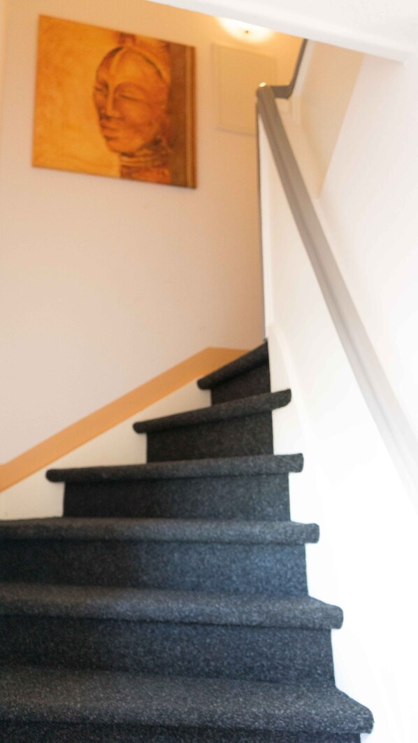 A staircase with dark steps and a wooden handrail, leading to a landing with a wall-mounted painting.