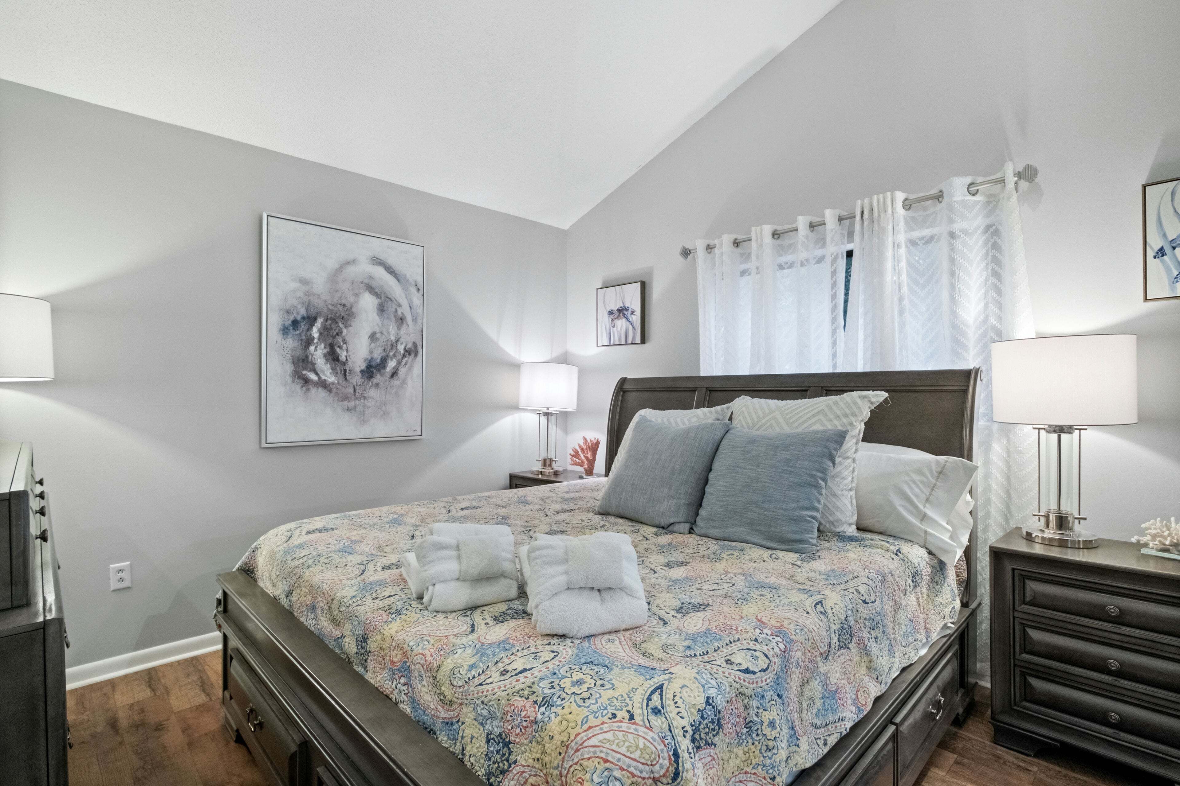Une chambre à coucher avec un grand lit, une table de chevet, une commode et une lampe fixée au mur.
