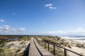 A wooden boardwalk leading to a beach with dunes and a clear sky.
