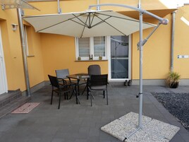 Un patio al aire libre con una mesa, sillas, una sombrilla grande y una planta en maceta.