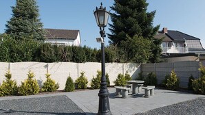 Um pátio pavimentado com um muro de pedra, um candeeiro e um banco.