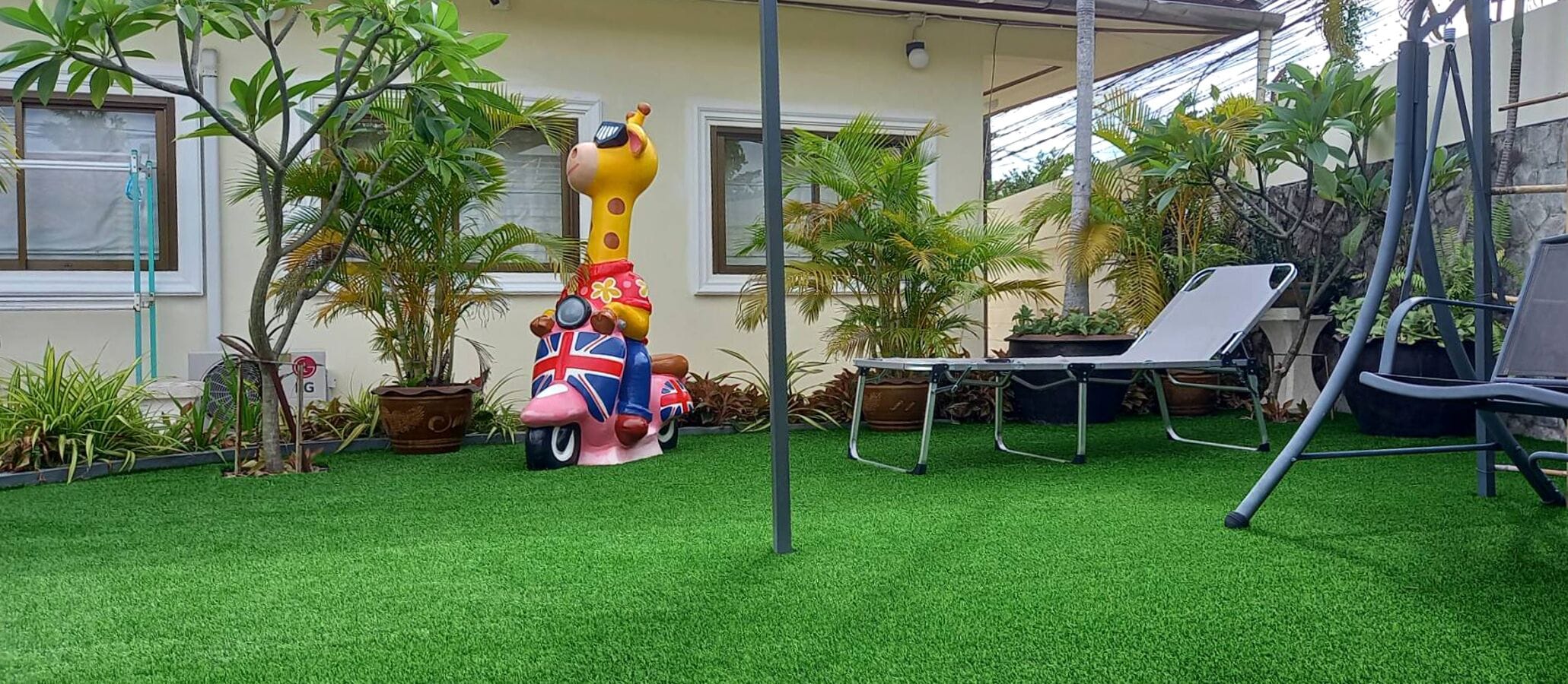 A backyard with artificial grass, a swing set, a lounge chair, and a decorative sculpture of a pig with a Union Jack flag.