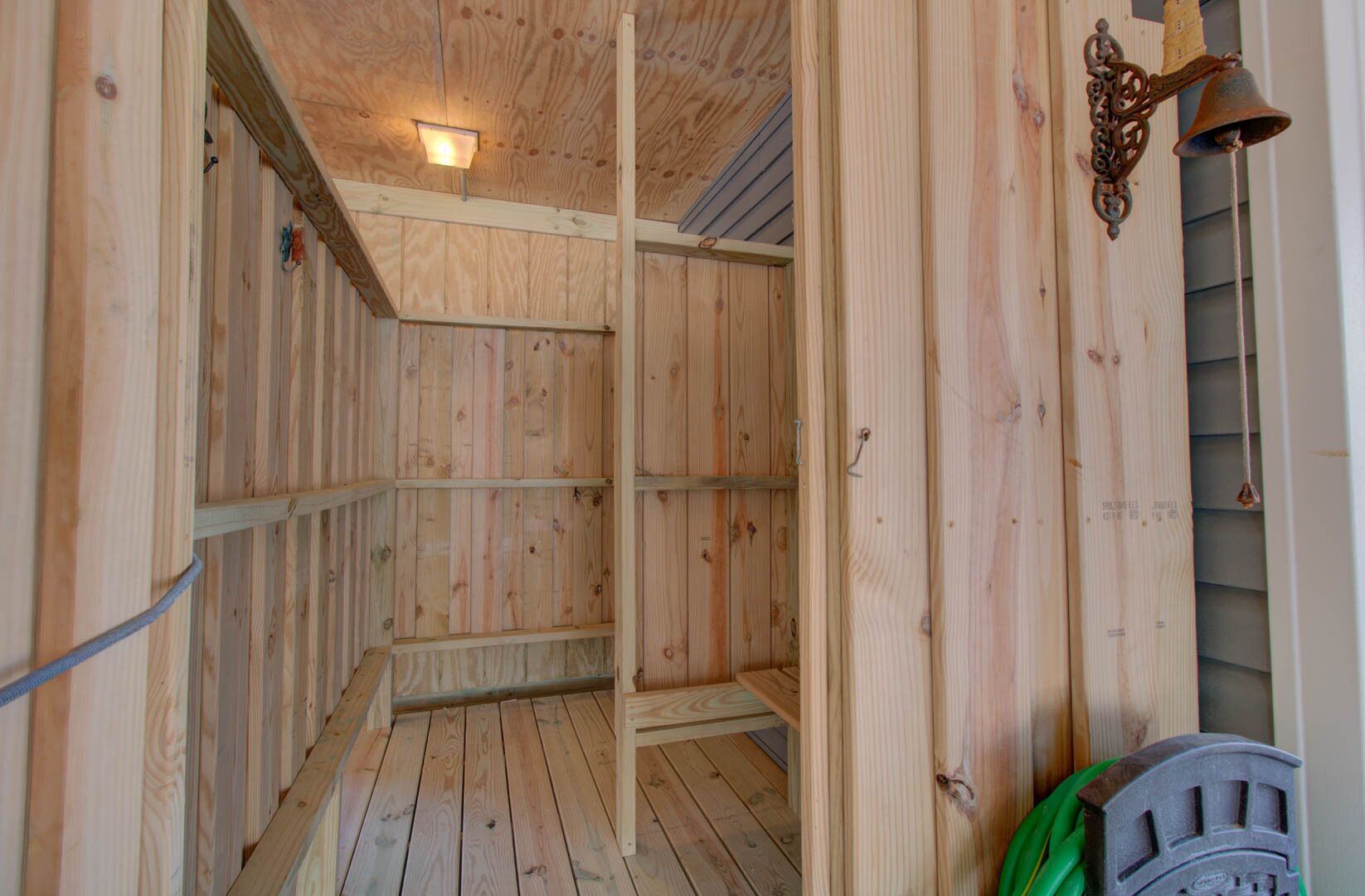 A wooden sauna with a sloped ceiling, a wall-mounted bell, and a green hose.