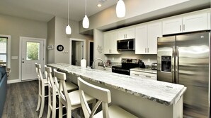 A modern kitchen with white cabinets, stainless steel appliances, and a marble countertop.
