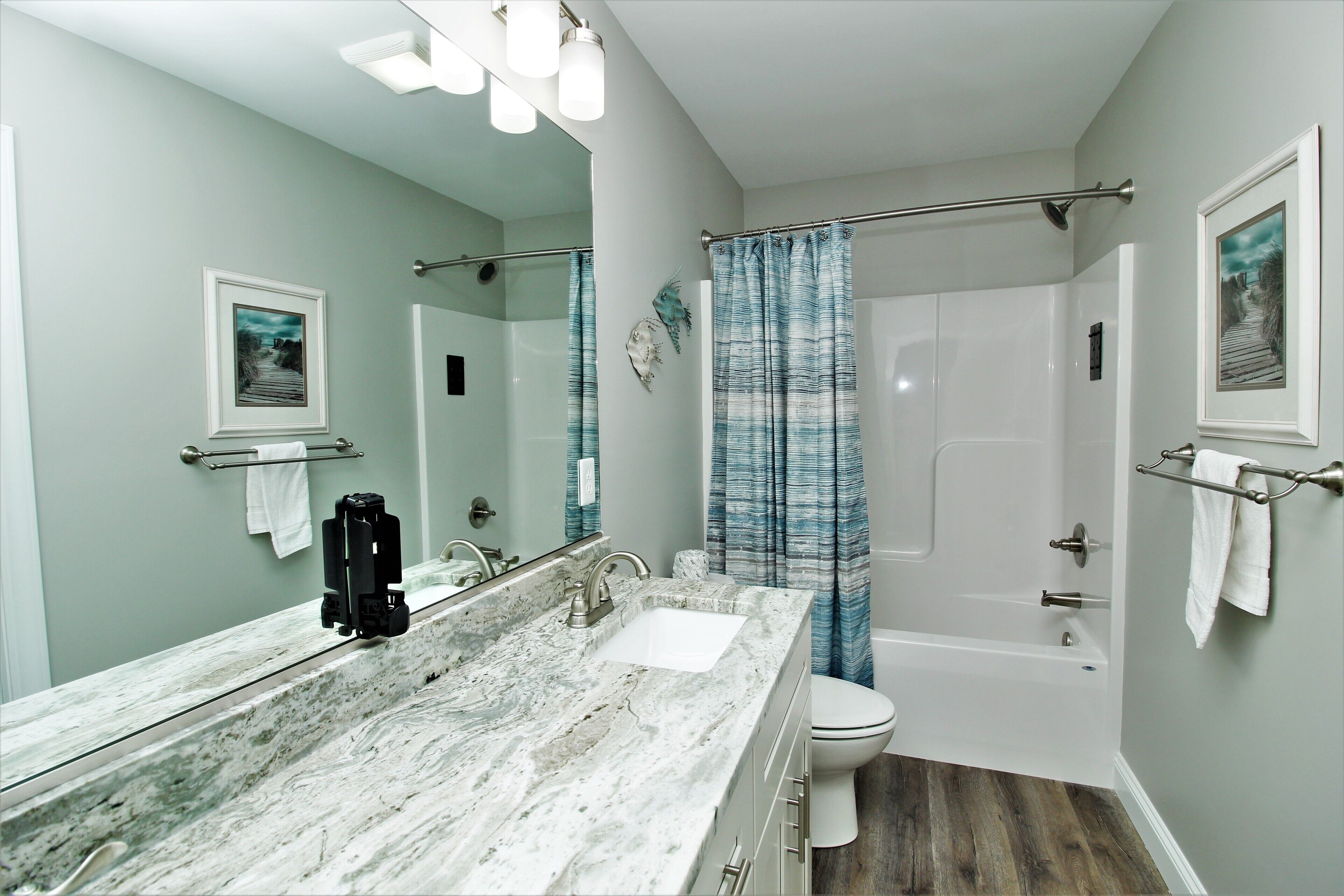 A bathroom with a marble sink, a large mirror, a shower with a curtain, and a toilet.
