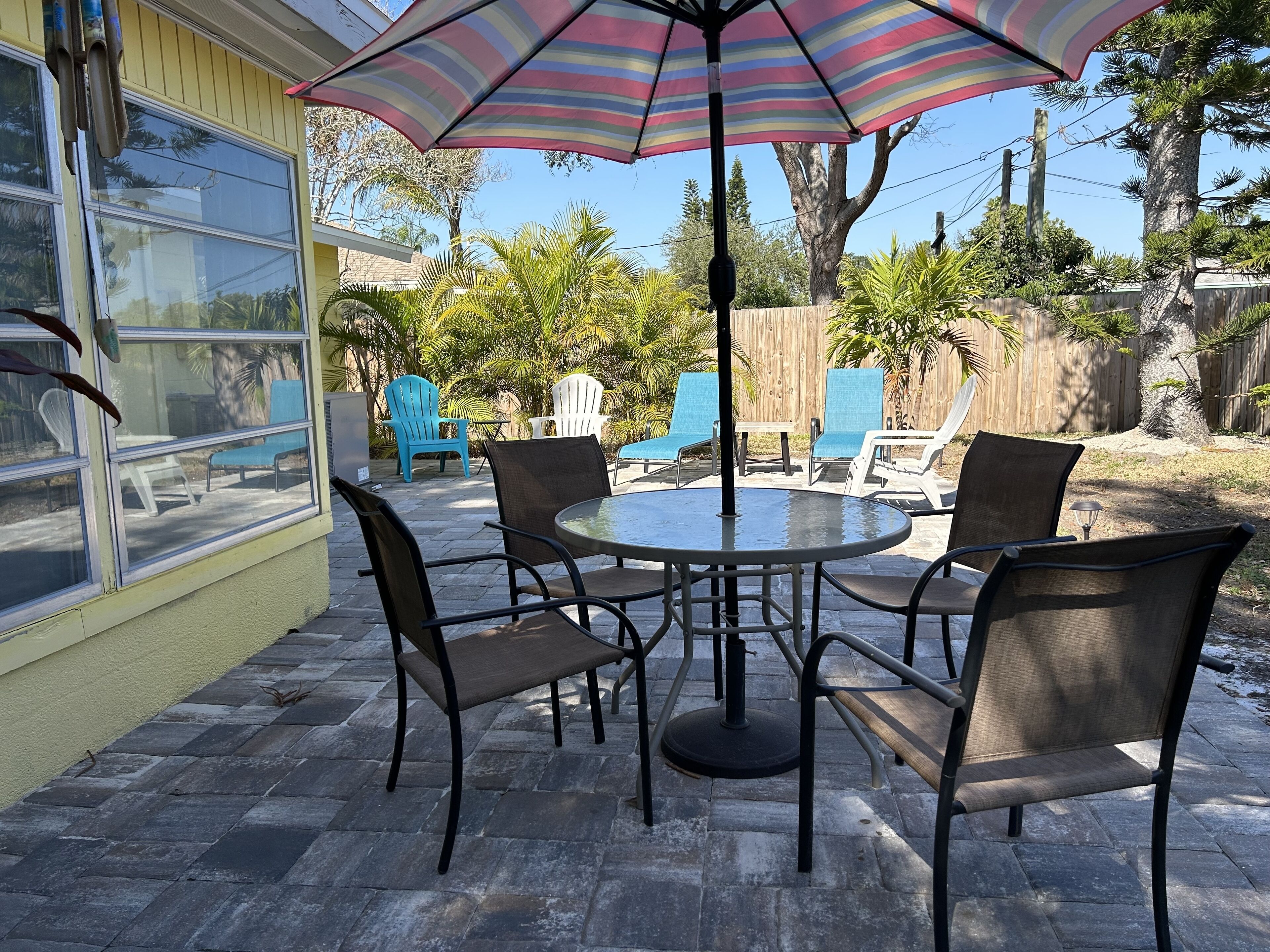 A patio with a round table and chairs, a striped umbrella, and a view of the backyard.