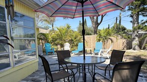 Eine Terrasse mit rundem Tisch und Stühlen, einem gestreiften Sonnenschirm und Blick auf den Garten.