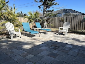 Eine Terrassenfläche mit drei Adirondack-Stühlen, ein blauer und zwei weiße, auf einem Pflasterboden.