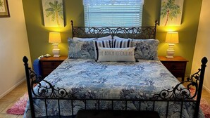 Ein Bett mit blauer Blumendecke, zwei Nachttischlampen, ein Nachttisch, ein rosa Teppich und ein Fenster mit Jalousien.