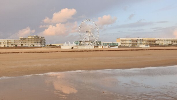 Une plage avec une grande roue et des bâtiments en arrière-plan.
