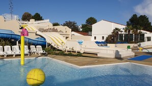 Un espace piscine doté d’un toboggan, de chaises longues et d’un panneau indiquant « TOBOGGAN ».