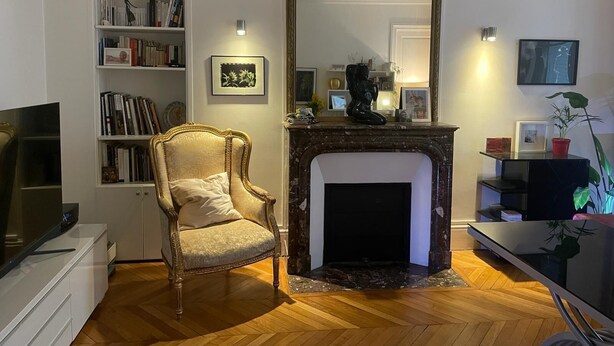 A living room with a fireplace, a bookshelf, a chair, and a television.