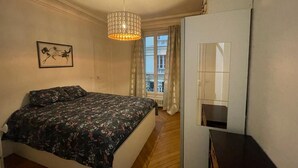 A bedroom with a bed, a hanging light fixture, a window with curtains, and a mirror.