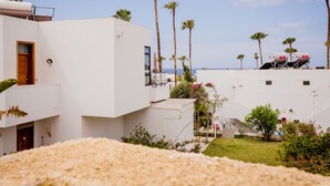 A modern white building with multiple balconies, palm trees, and a view of the sea.