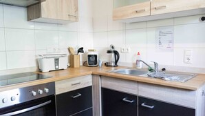 A modern kitchen with a toaster, coffee maker, and kettle on the counter, a sink with a faucet, and a stove. - Ferienwohnung Anke-Apartement 3c (Heinsberg)