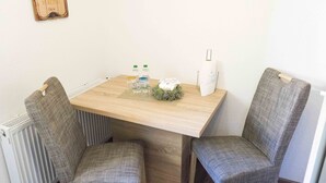 A small dining area with a wooden table, two upholstered chairs, a radiator, and a wall-mounted light fixture. - Ferienwohnung Anke-Apartement 3c (Heinsberg)