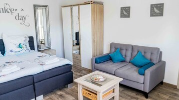 Un dormitorio con una cama, un sofá gris, una mesita y un espejo.