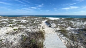 Een zandstrand met een houten looppad naar de oceaan.