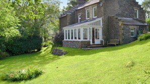 A stone house with a conservatory, surrounded by lush greenery. - 4 bedroom accommodation in Buttermere, near Keswick (Buttermere, near Keswick)