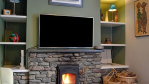 A living room with a stone fireplace, a flat-screen TV mounted above it, and shelves with various items. - 4 bedroom accommodation in Buttermere, near Keswick (Buttermere, near Keswick)