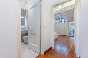 A hallway with a wooden floor leading to a bedroom with a bed and a window. - Pratello Elegante e Raffinata Mansarda (Bologna)