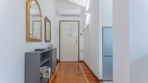 A hallway with a wooden floor, a grey cabinet with books, two mirrors, a door with a notice, and an air conditioner. - Pratello Elegante e Raffinata Mansarda (Bologna)