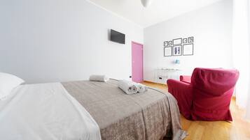 Habitación de hotel con cama, una puerta rosa, escritorio con lámpara y una silla roja.