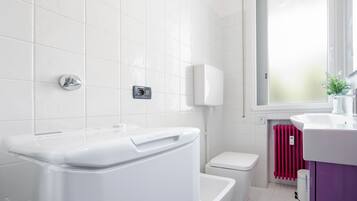 Ein modernes Badezimmer mit weißen Fliesen, einer weißen Toilette, einem weißen Bidet, einem weißen Waschbecken und einem Fenster mit Aussicht.