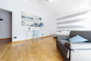 A modern living room with a grey sofa, a blue chair, and a small table. There are wall-mounted pictures and a ceiling fan. - Sant'Orsola Colorful Huge Apartment (Bologna)