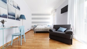 A modern living room with a glass desk, a blue chair, a grey sofa, and a bed with a white headboard. - Sant'Orsola Colorful Huge Apartment (Bologna)