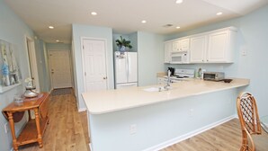 A kitchen with white cabinets, a white refrigerator, a microwave, and a wooden dining table. - TB 62C Updated 3 Bedroom 2 Bath Condo in True Blue Golf Community (Pawleys Island)