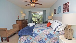 A bedroom with a bed, a chair, a dresser, a ceiling fan, and a view through a window. - TB 62C Updated 3 Bedroom 2 Bath Condo in True Blue Golf Community (Pawleys Island)