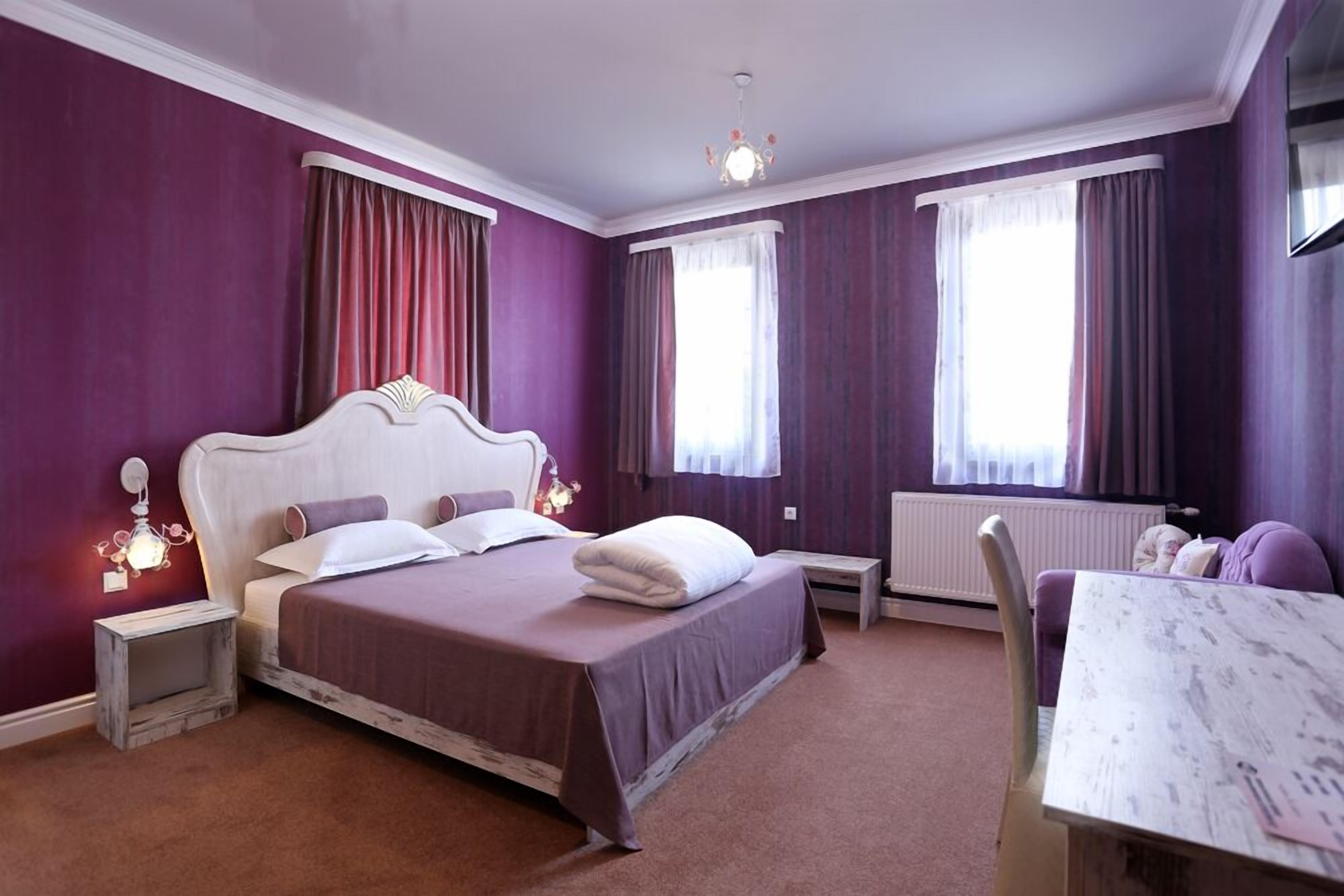 Une chambre à coucher avec un grand lit, deux tables de chevet, une commode, une coiffeuse, une chaise et une fenêtre avec des rideaux.
