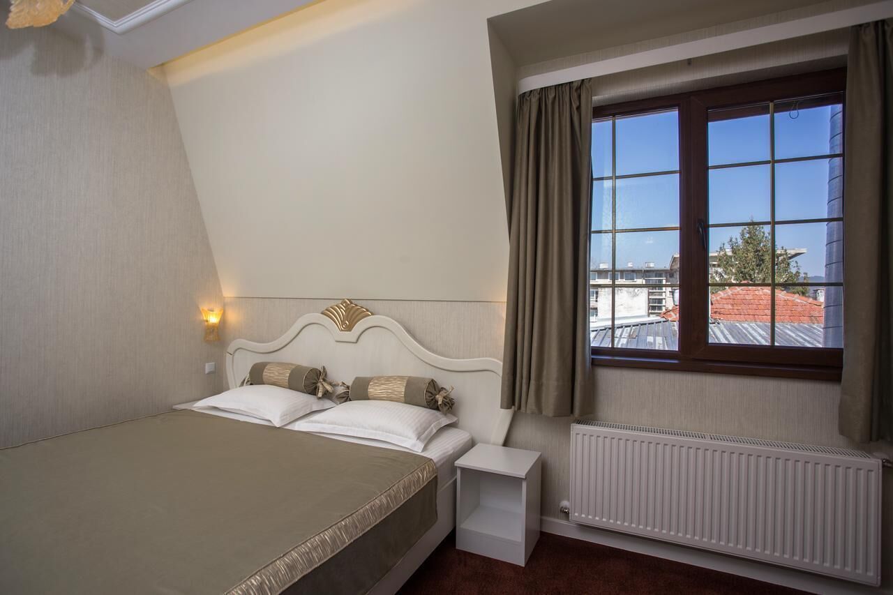 Un dormitorio con cama, mesita de noche, ventana con cortinas y radiador.