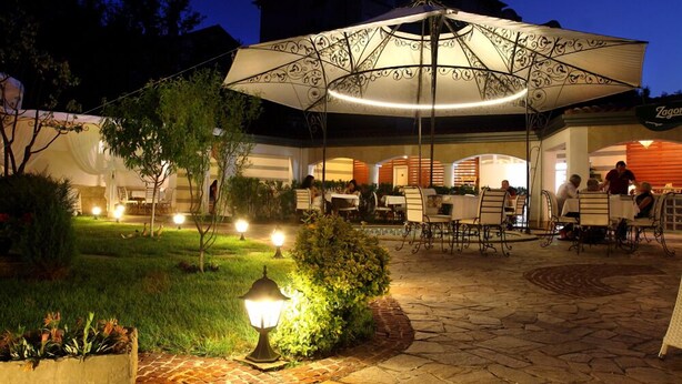 Un espace de restauration en plein air, avec des tables et des chaises, entouré de verdure et illuminé par un éclairage décoratif.