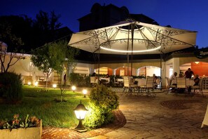 An outdoor dining area with tables and chairs, surrounded by greenery and illuminated by decorative lighting. - Hotel Green Garden (Shumen)