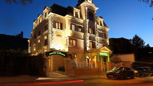 Un hôtel au style architectural classique, doté d’une entrée imposante avec une allée bordée de portails et d’un restaurant bien visible, appelé « Green Garden », situé au rez-de-chaussée.
