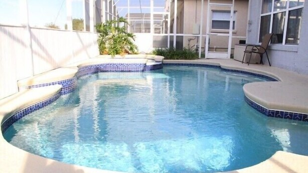 A swimming pool with a tiled edge, surrounded by a white wall and a small plant.