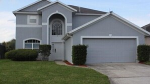A two-story house with a garage, a large arched window, and a well-maintained lawn.