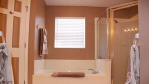 A bathroom with a bathtub, a glass shower enclosure, and a window with blinds.