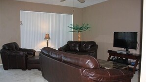 A living room with a brown leather sofa, a small table, a lamp, a television, and a plant.