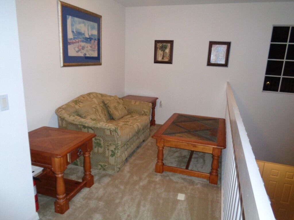 Una sala de estar con un sofá, dos mesitas de madera y una mesa de centro de vidrio.